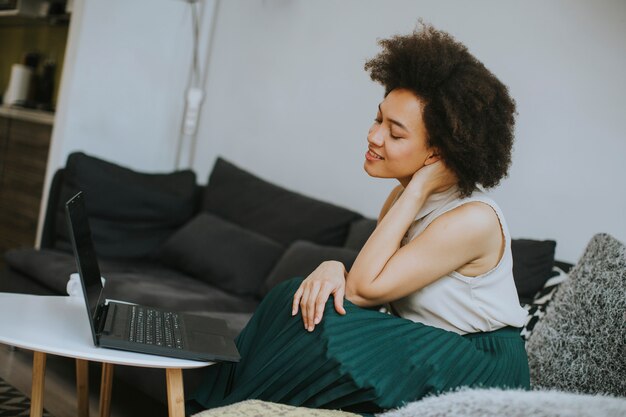 Young beautiful lady with curly hair work on the notebook while sit down on the couch at home