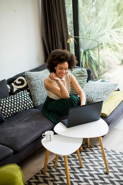 Young beautiful lady with curly hair work on the notebook while sit down on the couch at home