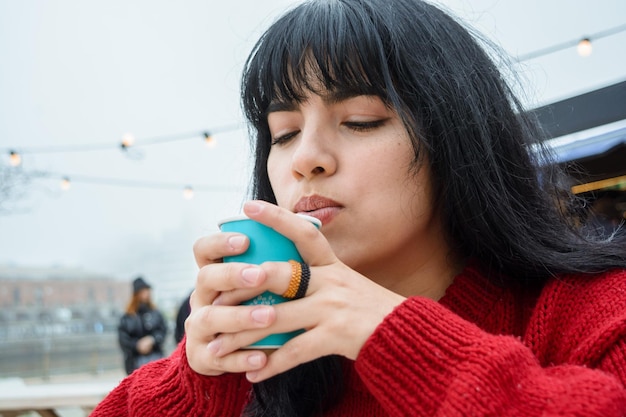 young beautiful latin woman outdoors having a hot drink on a cloudy and cold day