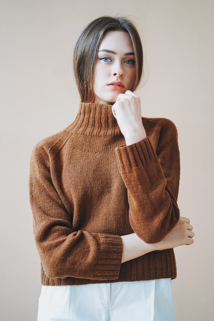 Photo ベージュ色の背景にカメラを見て茶色のニットのセーターに青い目を持つ若い美しい長い茶色の髪の髪の女の子
