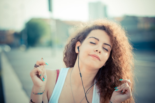 Foto musica d'ascolto della giovane donna dei bei capelli ricci lunghi dei pantaloni a vita bassa