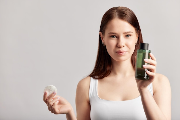 young beautiful longhaired girl applying a cleansing lotion to her face with a cotton pad caucasian brownhaired woman uses beauty products in skincare routine to keep her skin young and healthy
