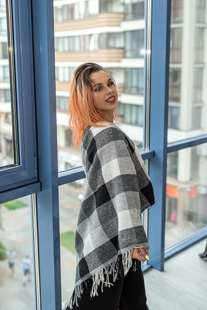 Young beautiful luxurious woman in a stylish outfit near a spacious large window in her apartment Shooting concept near the window