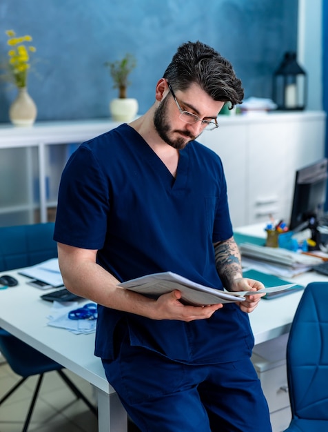 Young beautiful male doctor reading medical results at office. Modern hospital office background.