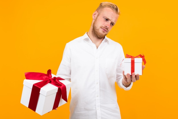 Young beautiful man holds two white boxes with gifts and chooses isolated on yellow