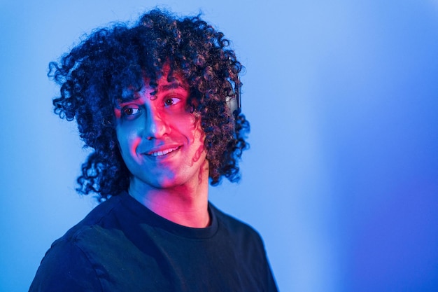 Young beautiful man with curly hair is indoors in the studio with neon lighting