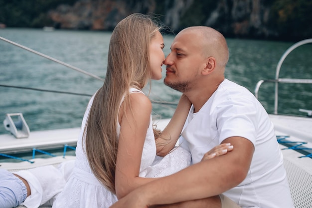 Young beautiful married couple kissing on the yacht on\
vacation. caucasian woman with long hair and bald man in the\
andaman sea. phuket.