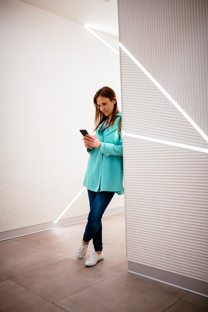 Young beautiful middle-aged woman typing with smartphone leaning against a wall. business.