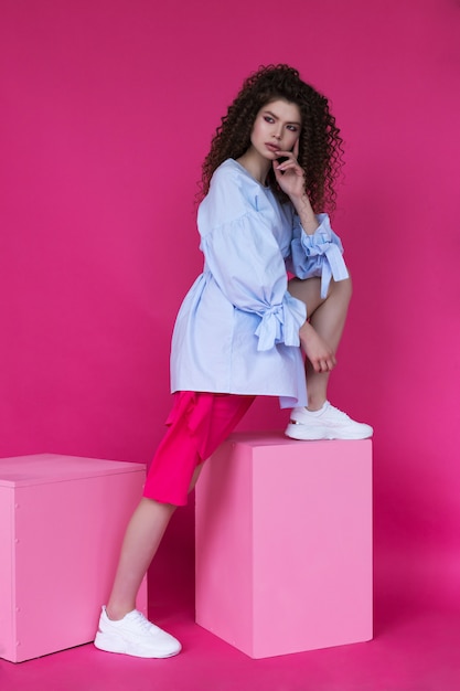 Young beautiful model with afro curls hairstyle wearing blue blouse on pink 