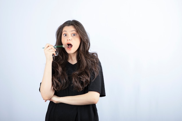 Young beautiful model with brush feeling surprised on white wall. 