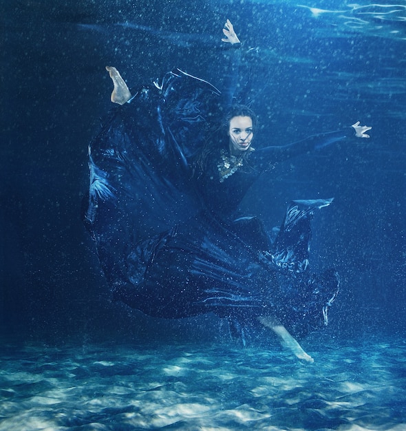 The young beautiful modern dancer in long dress dancing under water drops in blue aqua