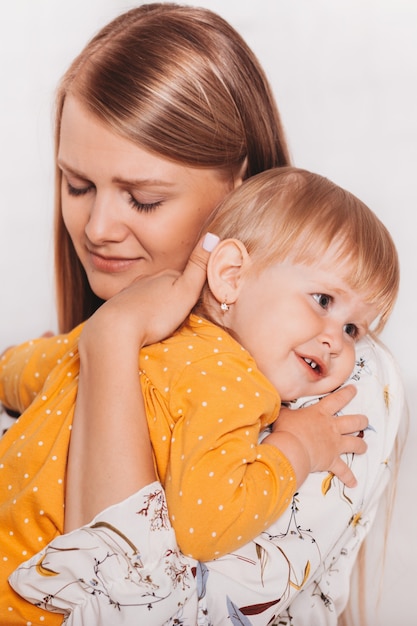 Young beautiful mom gently hugs her little daughter. Vertical