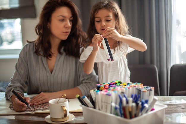 Young beautiful mother and cute daughter draw a mandala pattern together artistic markers and colore...