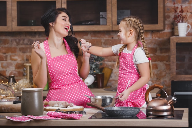 若い美しい母親と彼女の小さな娘が一緒にキッチンで料理