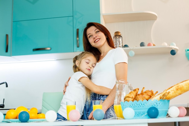 Young beautiful mother and her little daughter playing in the kitchen during breakfast at home.