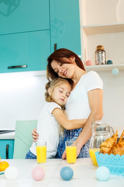 若い美しい母親と彼女の小さな娘は、自宅で朝食時にキッチンで遊んでいます。