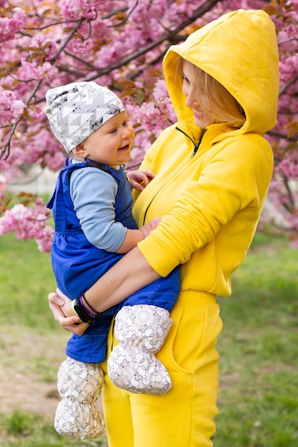 若い美しい母親は、花の咲く庭で小さなかわいい息子のお母さんと小さな男の子を腕に抱きますさくら