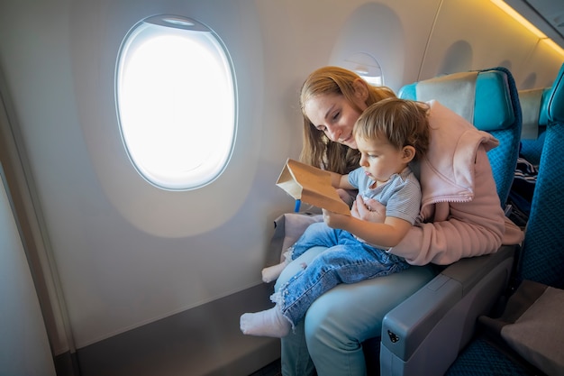 Young beautiful mother and little cute toddler sit in an airplane chair open a cardboard bag