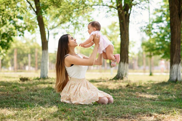 Young beautiful mother playing with a baby on the grass in a park.