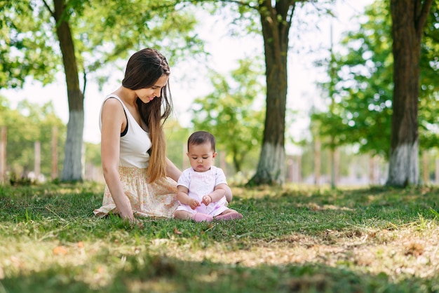 Young beautiful mother playing with a baby on the grass in a park.