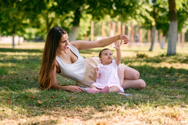 Young beautiful mother playing with a baby on the grass in a park.