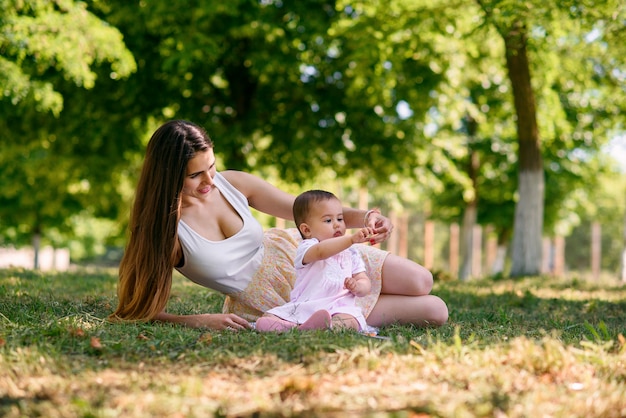 Young beautiful mother playing with a baby on the grass in a park.