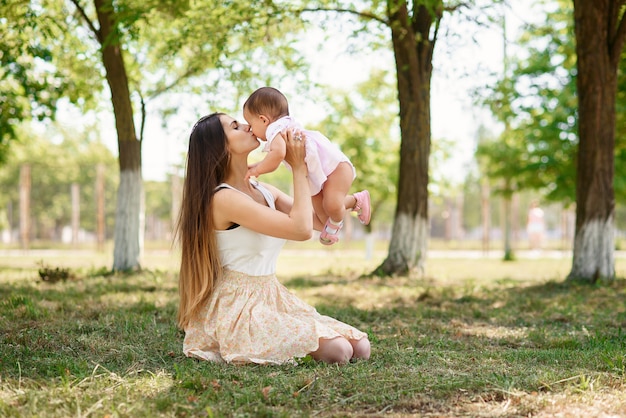 Young beautiful mother playing with a baby on the grass in a park.