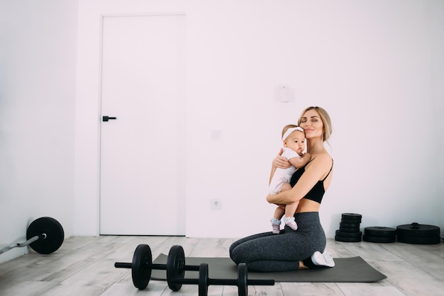 Young beautiful mother with her daughter in her arms sits in the room on the floor after yoga exercises Doing sports at home