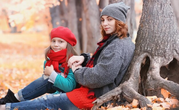 Young beautiful mother with her daughter on nature. a girl in a hat walks in park. girl in autumn city park in leaf fall