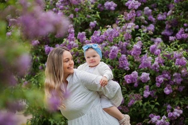 Young beautiful mother with little daughter 15 years old in blooming lilacs Happy family in the park Spring