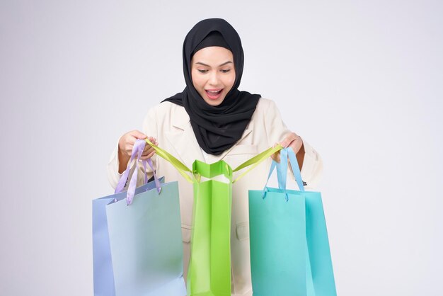 Young beautiful muslim woman in suit holding colorful shopping bags over white background studio