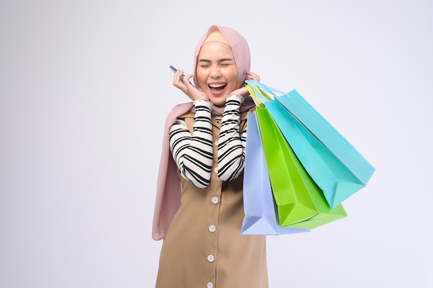 Young beautiful muslim woman in suit holding colorful shopping bags over white background studio