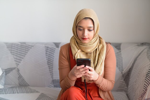 Young beautiful Muslim woman using phone in the living room at home