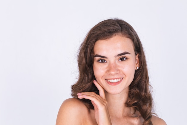 Young beautiful natural soft clean skin woman with freckles light makeup on white wall with bare shoulders