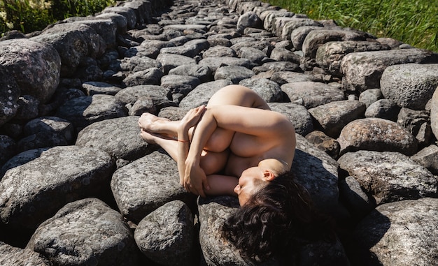 石防波堤でポーズをとる若い美しい裸の女性。自然を楽しむ裸のブルネット