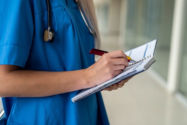 젊고 아름다운 간호사는 유니폼, 마스크, 장갑, 청진기를 입고 복도에 서서 태블릿을 들고 있습니다. 의학 개념