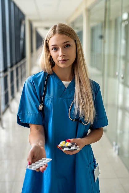 Young beautiful nurse stands in the hallway with a stethoscope and pills in her hands Medicine concept