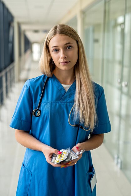 Young beautiful nurse stands in the hallway with a stethoscope and pills in her hands