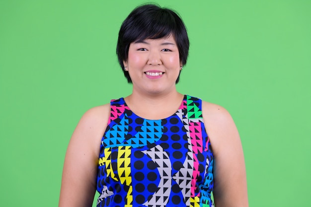  young beautiful overweight Asian woman ready to party against chroma key with green wall