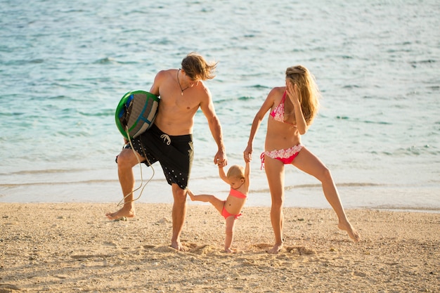 Genitori giovani e belli che giocano con sua figlia sulla spiaggia