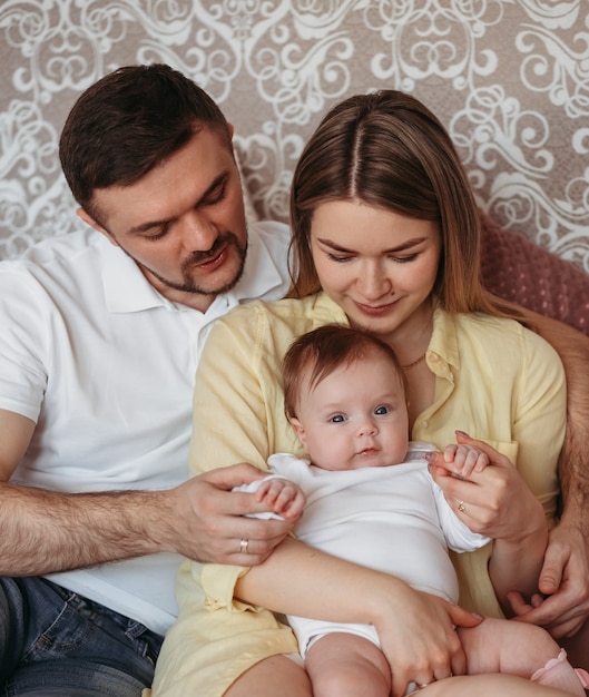 Young beautiful parents with newborn daughter in their arms look at the baby