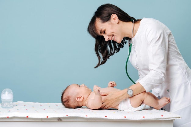 A young beautiful pediatrician examines the baby in a diaper and smiles at him. Isolated not blue background