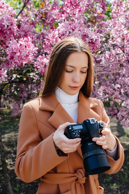 若い美しい写真家が歩いて、庭で写真を撮る