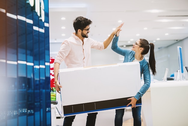 Photo young beautiful playful couple is celebrating buying a new tv by high-fiving.