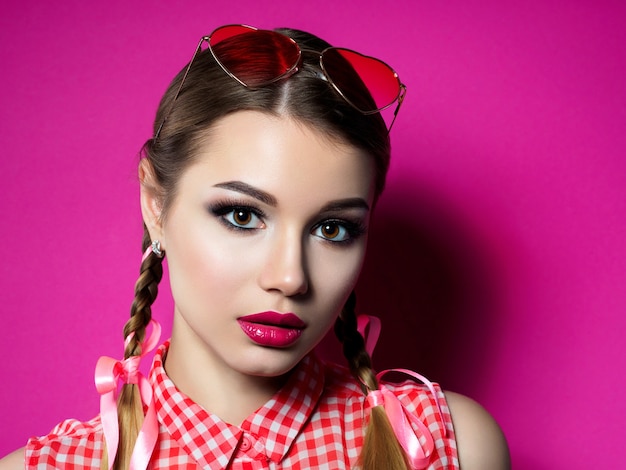 Young beautiful playful woman looks over her heart shaped red glasses. Valentines day, love or pinup theme party concept. Smokey eyes and red lips makeup. 