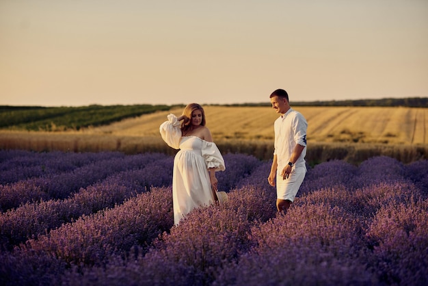 Giovane bella coppia incinta che cammina su un campo di lavanda al tramonto concetto di famiglia felice