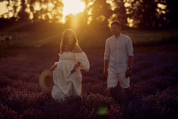 Giovane bella coppia incinta che cammina su un campo di lavanda al tramonto concetto di famiglia felice