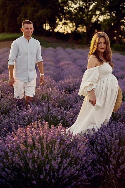 Young beautiful pregnant couple walking on a lavender field at sunset Happy family concept