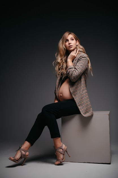 Young beautiful pregnant woman in jacket on black wall