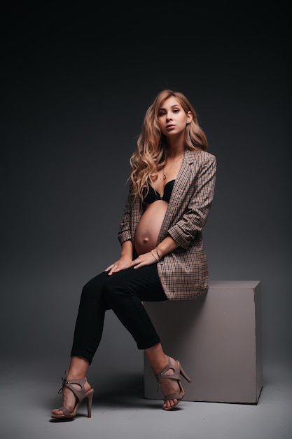 Young beautiful pregnant woman in jacket on black wall